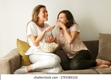 Two beautiful friends watching tv show and eating popcorn at home - Powered by Shutterstock