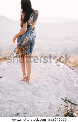 two beautiful girlfriends in summer dress with patterns of light walking and posing near the rocks on the sand at sunset. the wind in her hair