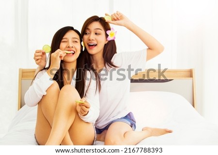 Two beautiful girls beauty at home : Portrait beautiful and cute buddy couple. Asian spa easily at home sitting in bed eating cucumber slices relaxing teasing some fun skin and wellness. 