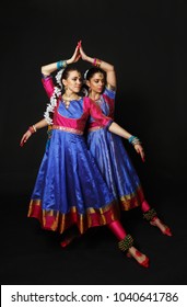 Two beautiful girls dance in Indian costumes. Indian dance in studio on a black background.