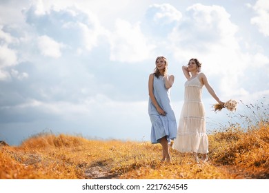 Two beautiful girls in dresses in autumn field have fun