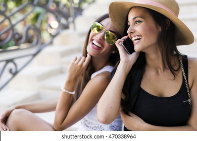 Two beautiful girls laughing while talking on phone with a boy