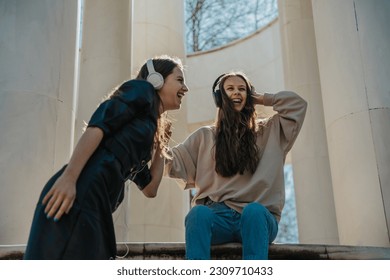 Two beautiful girls listening to music on their headphones and laughing. Enjoying the summer day in the park - Powered by Shutterstock