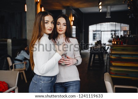 two beautiful girls standing in a cafe and drinking coffee
