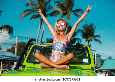 Two Beautiful Girls In Swimsuits And Sunglasses Travel On An SUV, An Off Road Car On A Tropical Island, A Summer Trip, A Fashionable Photo