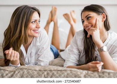 Two beautiful girls talking and smiling while lying on a luxurious  bed - Shutterstock ID 272540687