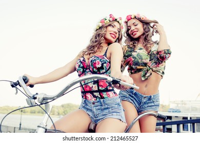 Two Beautiful Girls Twins Ride On A Tandem Bike Outdoors