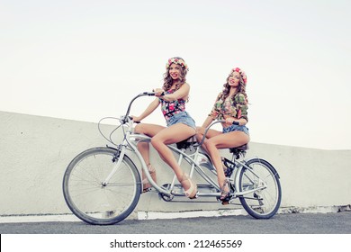 Two Beautiful Girls Twins Ride On A Tandem Bike Outdoors