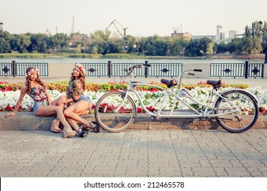 Two Beautiful Girls Twins Ride On A Tandem Bike Outdoors