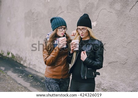 two beautiful girls walk around town fashionably and stylishly dressed with a Cup of coffee