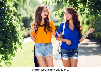 Two Beautiful  Girls Walking In  The  Summer Park End Talking.  Friends Wearing Stylish Shirt And Jeans Shorts , Enjoying  Day Off And Have Fun.