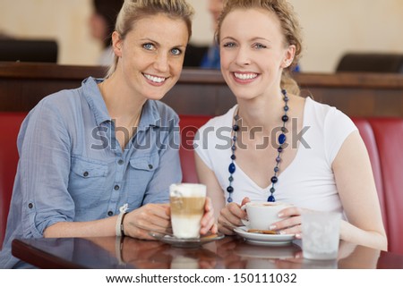 Two beautiful happy female friends enjoying a cup of cofee at a cafeteria