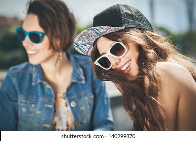 Two Beautiful Happy Girls In Sunglasses On The Urban Background. Young Active People. Outdoors