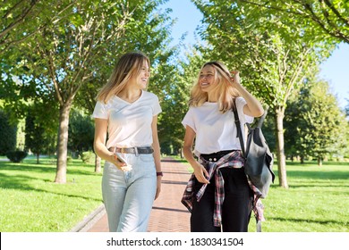 Two Beautiful Happy Girls Teenagers 17, 18 Years Old Walking Together In Park, Girls Laughing Talking Having Fun On Sunny Summer Day