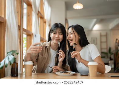 Two beautiful and happy young Asian women are enjoying taking pictures together with a smartphone while hanging out at a cozy coffee shop. people, lifestyles, wireless technology - Powered by Shutterstock