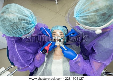 two beautiful helpers in special clothes masks hats gloves help to conduct the operation to the dentist. The concept of dental surgery
