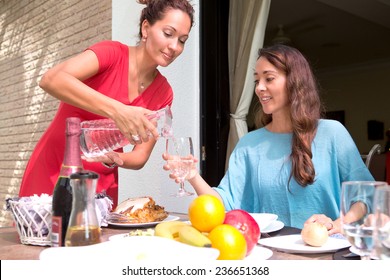 Two beautiful hispanic women enjoying an outdoor home meal together, one pouring water into a glass. - Powered by Shutterstock