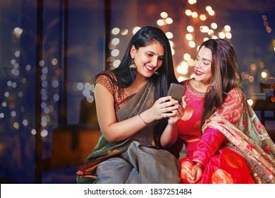 Two Beautiful Indian Women In Ethnic Clothes Doing Diwali Shopping Online, Using App On Mobile Phone