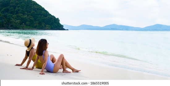 Two Beautiful Lgbt Lesbian Female Friends Relax And Happy At The Beach Sitting On The Sand Wearing Swimsuit. Travel At Island Beach And Sea Ocean On Holiday Vacation.