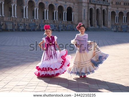 Two beautiful little girls dancing flamenco dressed in typical gypsy costume holding their dress with one hand in a famous square in seville. Flamenco, cultural heritage of humanity