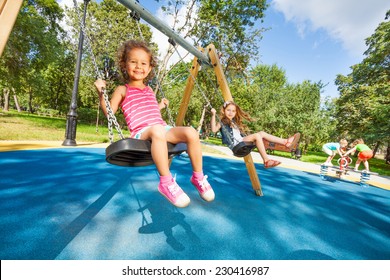 Two beautiful little girls swinging on swings on playground with smile on sunny summer day - Powered by Shutterstock