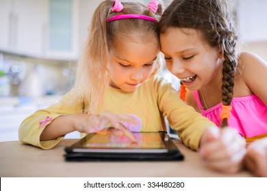 Zwei schöne kleine Schwestern sitzen an einem Tisch und spielen auf einem Tablet PC.