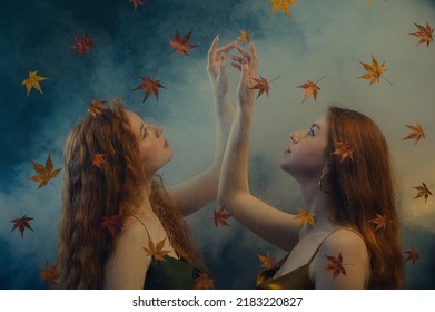 Two beautiful redhead freckled women with long natural curly hair posing in smoke, darkness and warm light. Art studio portrait made through the wet glass with red autumn leaves. Film grain effect  - Powered by Shutterstock