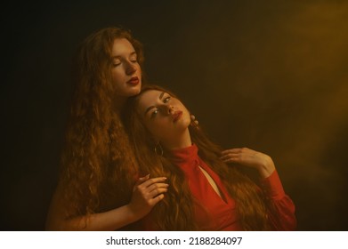 Two Beautiful Redhead Freckled Women With Long Natural Curly Hair, Red Lips Makeup Posing In Darkness And Warm Light. Studio Art Portrait. Copy, Empty Space For Text 