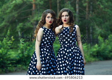 Two beautiful sisters girls with makeup and hairdo in summer park with surprised emotions on face
