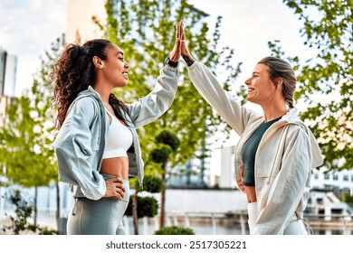 Two beautiful sporty fit women a high five each other in the park in the morning. Preparation for running, teamwork, motivation, healthy lifestyle. - Powered by Shutterstock