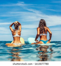 Two beautiful sporty surfing girl in sexy bikini sit on a big longboard surf surfboard board and wait for big wave on sunrise or sunset in the ocean. Modern active sport lifestyle and summer vacation.