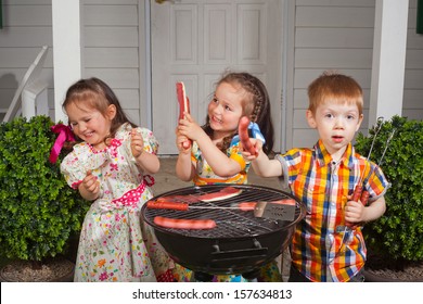 Two Beautiful Twin Girls And One Red Head Boy Eating Barbecue And Playing In Summer Garden