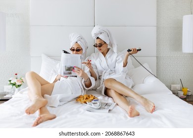 Two beautiful woman in bathrobe reading magazine, having fun and calling room service - Powered by Shutterstock
