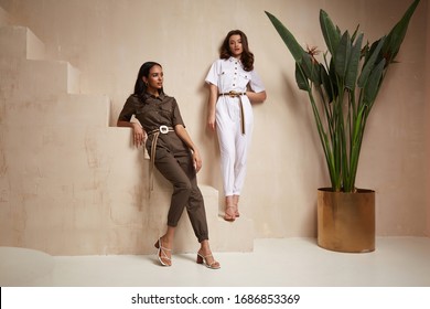 Two beautiful woman fashion model brunette hair friends wear overalls suit casual style sandals high heels accessory clothes safari Sahara journey summer hot collection plant flowerpot wall stairs.