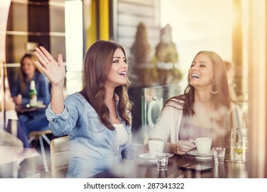 Two Beautiful Women Drinking Coffee And Chatting In Cafe