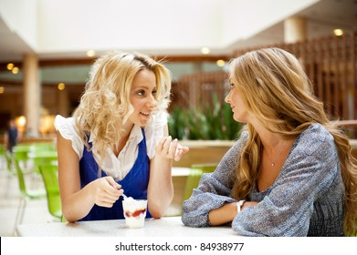 Two Beautiful Women Drinking Coffee And Chatting At Mall Cafe.