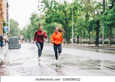 Two Beautiful Women Running In City With Rain And Puddles.