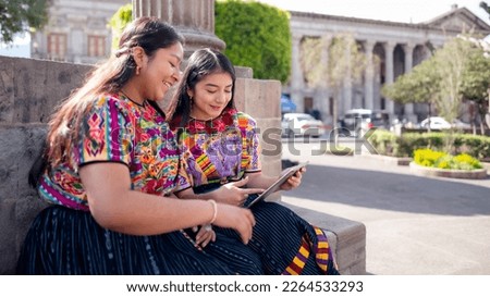 Two beautiful women sitting in a local park, watching online content.