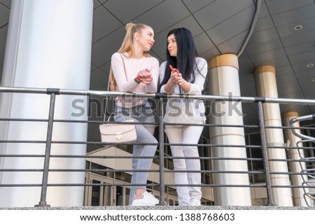 two beautiful women talking leaning on the railing of a modern building