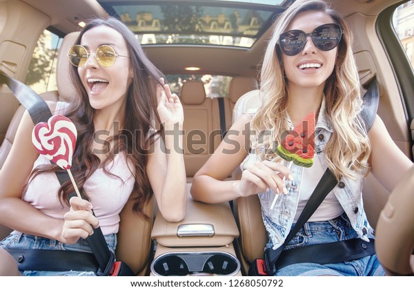 two beautiful women wearing sunglasses holding big
lollipops in the car