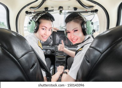 two beautiful young Asian pilot student looking at the back seat holding up thumb, wearing their uniform and headsets. In small light aircraft ready to take off - Powered by Shutterstock