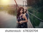 two beautiful young girlfriends blonde and brunette embracing on lake bridge on evening sunet. Rural scene. Women lesbians, hugging each other