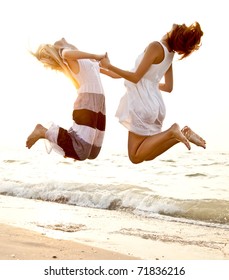 Two beautiful young girlfriends jumping on the beach at sunset. Photo with counter-light on background.