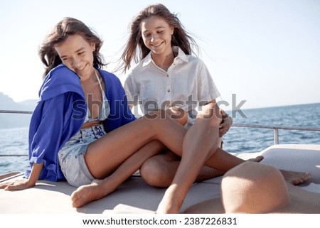 Two beautiful young girls with a slender figure travels and rests on a boat during a summer vacation in the open sea or ocean against the background of the island.   Friends tiurists tigether