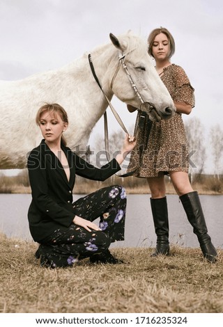 two beautiful young girls walking in an empty field with a horse