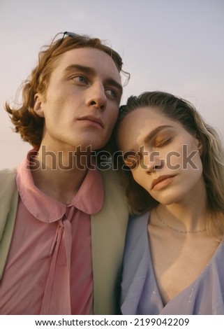 Two beautiful young models walk on the road. Blonde woman and redhead man. Stylish couple in retro clothes. Suburb area. Soft light, nice colors. Summer landscape, sunset.