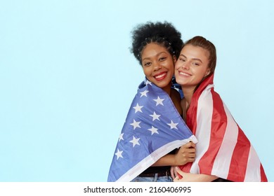 Two beautiful young multiethnic women are wrapped in the Usa flag and looking at the camera on a blue background with copy space. Celebrate independence day - happy 4th of july. - Powered by Shutterstock