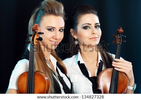 two beautiful young woman with violins over dark background