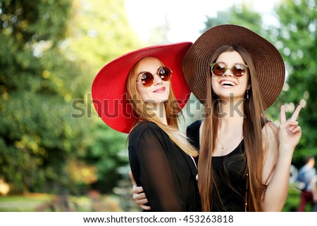 Two beautiful young woman wearing hippie boho style, with a wide-brimmed hat and stylish sunglasses, having fun on summer music festival