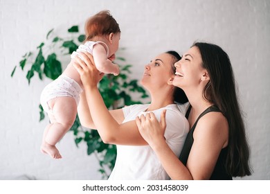 Two beautiful young women in casual clothes hug and look at their little child in the apartment. the concept of lgbt people. lesbian marriage and adoption, homosexuals-a lesbian couple.